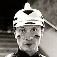 Schwarzweißaufnahme. Portrait eines Mannes, der eine wie ein Fußball gemusterte Pickelhaube auf dem Kopf trägt, seine Wangen sind mit der Deutschlandflagge bemalt.
