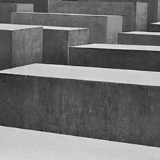 Schwarzweißaufnahme: Denkmal für die ermordeten Juden Europas, rechts an eine Stele gelehnt eine Frau mit Regenschirm.